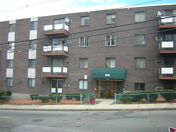 Front view of a multi-story brick apartment building with balconies and an entrance canopy.