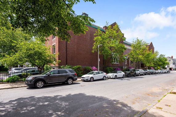 Side view of a large brick building with parked cars along the street.