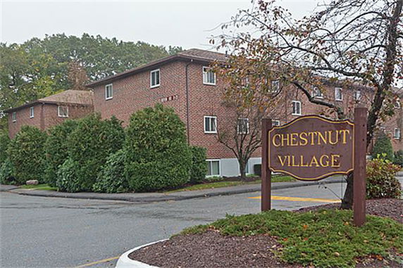 Front view of a brick apartment building with a sign reading 'Chestnut Village'.