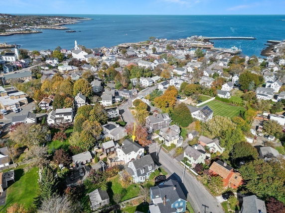Aerial view of a coastal town with numerous houses and a shoreline, including a harbor in the background.