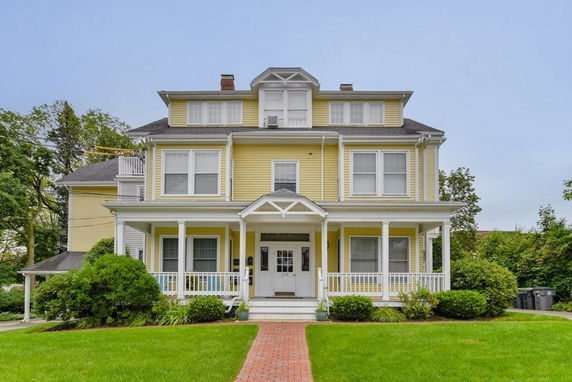 Front view of a two-story traditional house with a porch and yellow siding.
