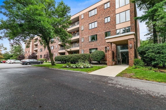 Front view of a multi-story brick apartment building with balconies and an entrance walkway.