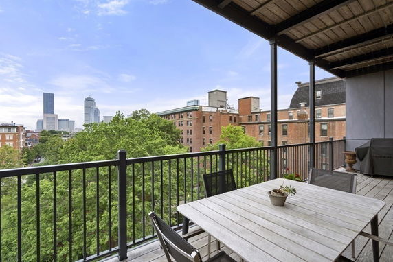 Panoramic view from a building's balcony showing city skyline and nearby trees.