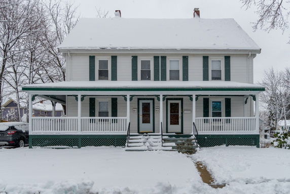 Front view of a two-story house with a covered porch and snow on the roof.