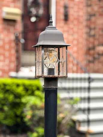 Close-up of an outdoor lamp post with a house in the background.