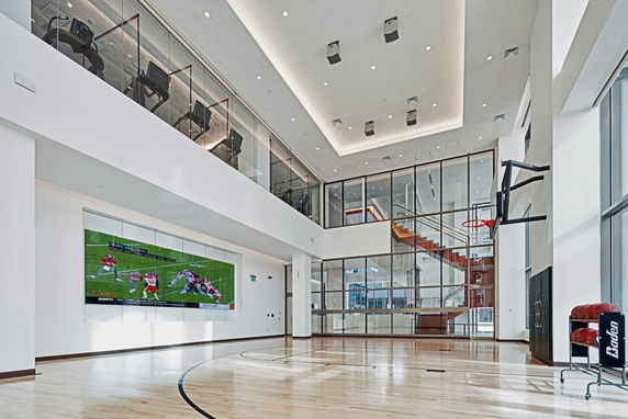 Indoor basketball court with a large TV screen on the wall and modern furnishings.