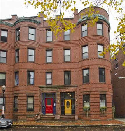 Front view of a historic multi-story brick building with rounded corners and colorful doors.