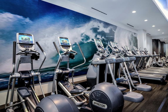 Indoor gym area with exercise equipment and a mural of ocean waves on the wall.