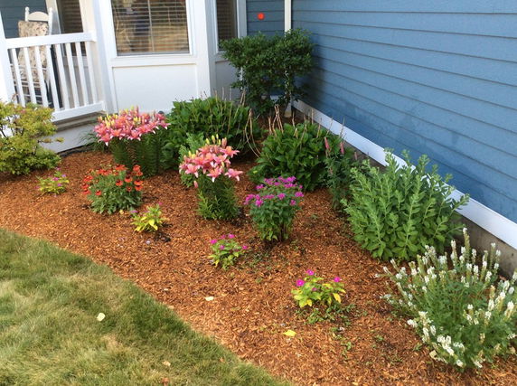 Partial view of a house with blue siding, white trim, and a garden with various flowering plants.