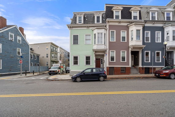 Front view of a row of multi-story townhouses with distinct colored facades, featuring bay windows and dormers.