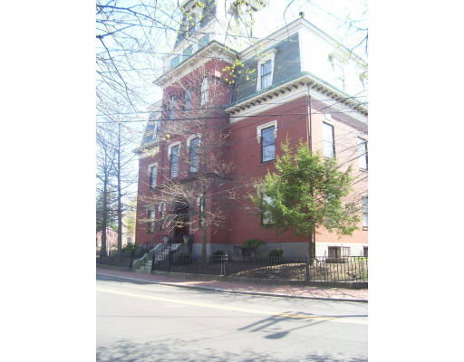 Front view of a large brick building with multiple stories and a pointed roof.