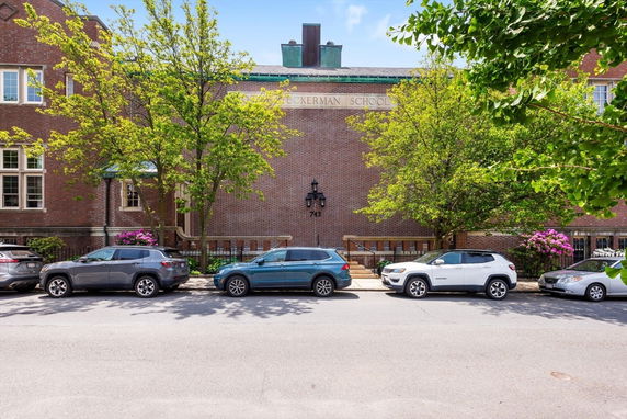 Front view of a brick building with trees and parked cars.