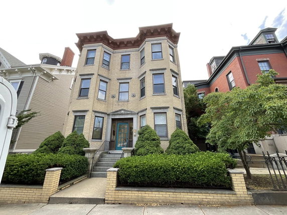 Front view of a multi-story house with a brick facade and decorative windows.