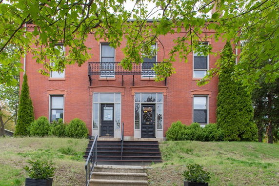 Front view of a two-story brick house with a symmetrical facade and stairway leading to the entrance.
