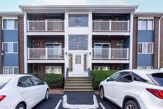Front view of a multi-story residential building with balconies and adjacent parked cars.