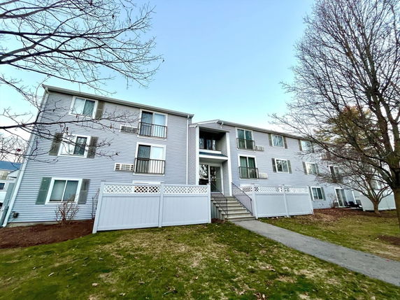 Front view of a multi-story residential building with balconies and stairs leading to the entrance.