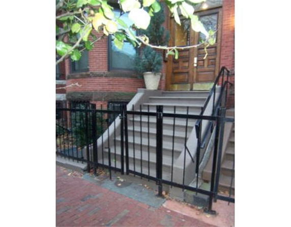Front view of a brick building with a staircase and wooden door.