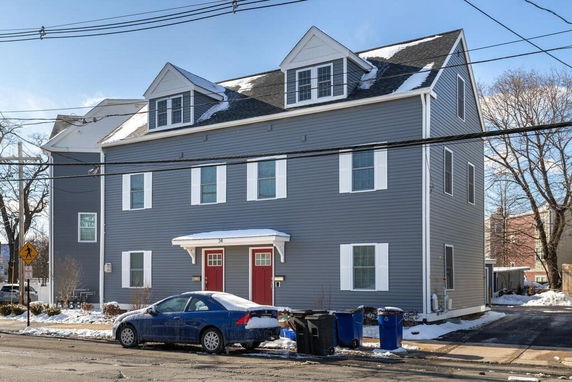 Front view of a dark gray multi-story house with white trim and red doors.