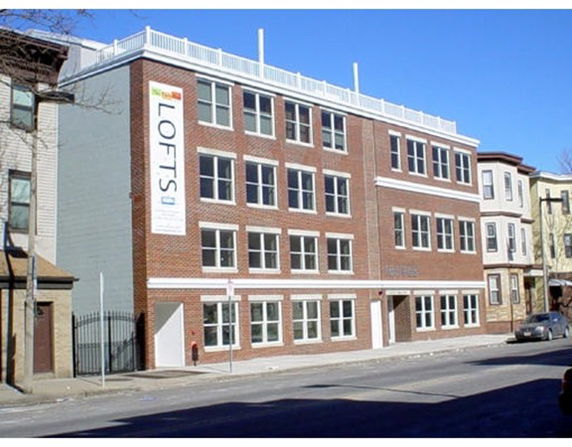 Front view of a multi-story brick building with multiple windows and a rooftop railing.