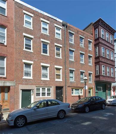 Front view of a four-story brick building with multiple windows and parked cars along the street.
