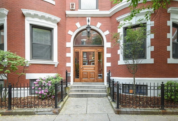 Front view of a brick building with arched wooden door and decorative windows.