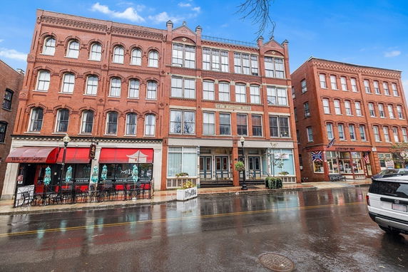 Front view of a four-story brick building with shops on the ground floor.