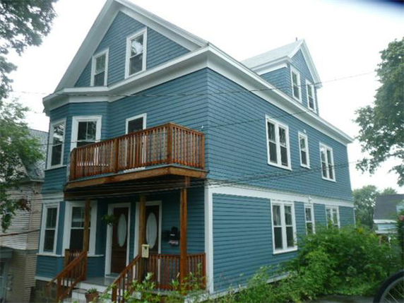 Front view of a multi-story blue house with a wooden balcony.