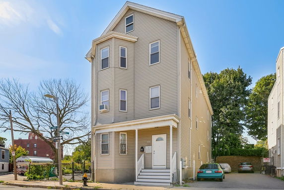 Front view of a tall three-story house with a small porch and an exterior staircase.