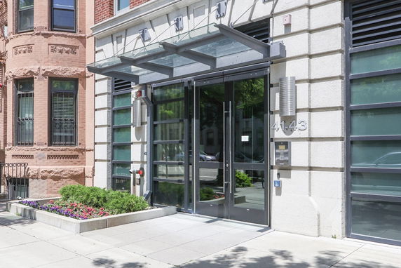 Front view of a modern building entrance with glass doors and a metal canopy.