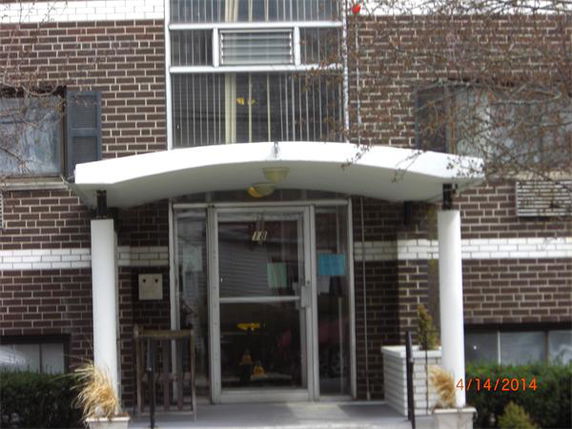 Front view of a brick apartment building entrance with a white awning and glass doors.