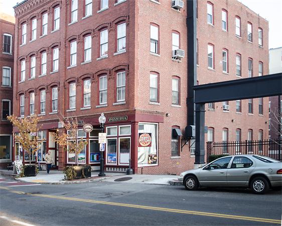 Front view of a multi-story brick building with a pizzeria on the ground floor.