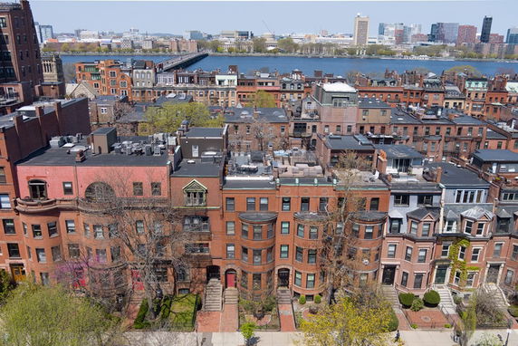 Aerial view of a row of multi-story brick buildings with a river and cityscape in the background.