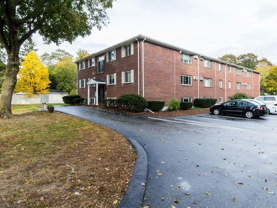 Front view of a multi-story brick building with adjacent parking area.