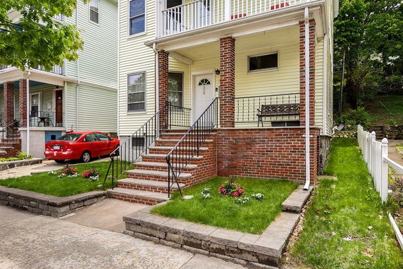 Front view of a multi-story house with stairs leading to the entrance and brick accents.