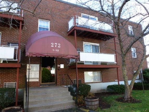 Front view of a brick apartment building with balconies and an entrance canopy labeled '272'.