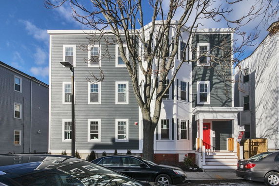 Front view of a multi-story residential building with multiple windows and a porch with red door.