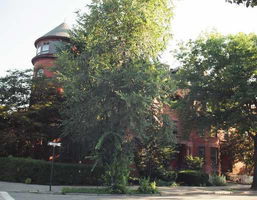 Front view of a large red brick building with a round tower and a conical roof.