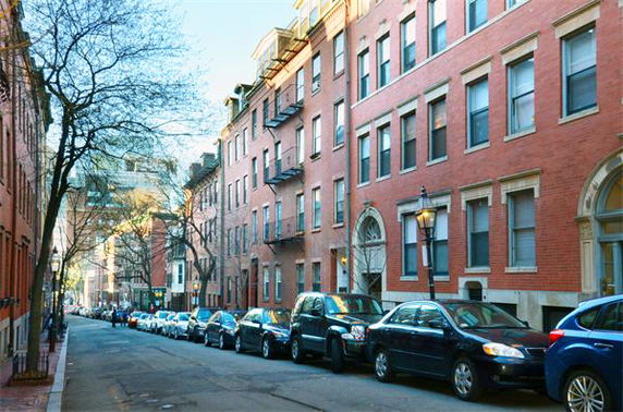 Elevated view of a street lined with red brick buildings and parked cars.