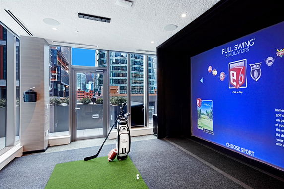 Indoor golf simulation room with large screen and sports equipment.