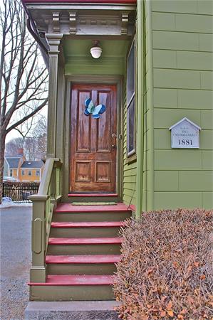 Front view of a house with green siding and a wooden door, marked with the year 1881.