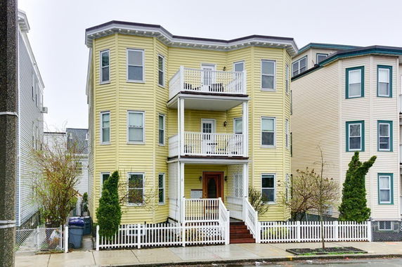 Front view of a three-story yellow house with balconies and white trim.