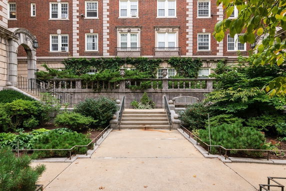 Front view of a multi-story brick building with greenery and stone steps.