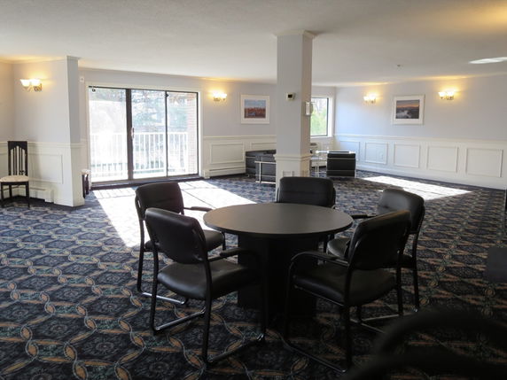 Interior view of a room with chairs and a table, featuring large windows and wall decor.