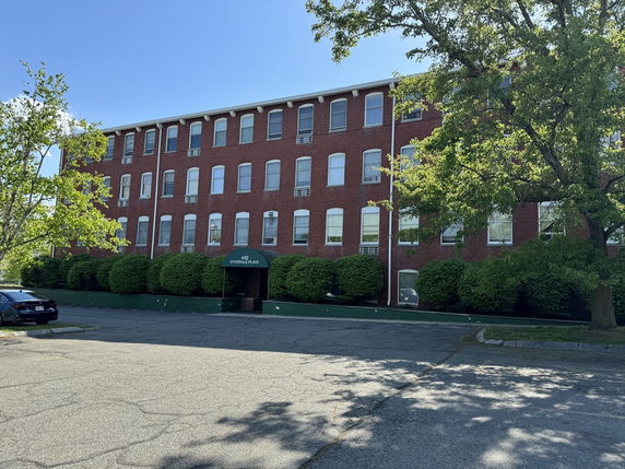 Front view of a large, four-story brick building with numerous windows and an entrance canopy.