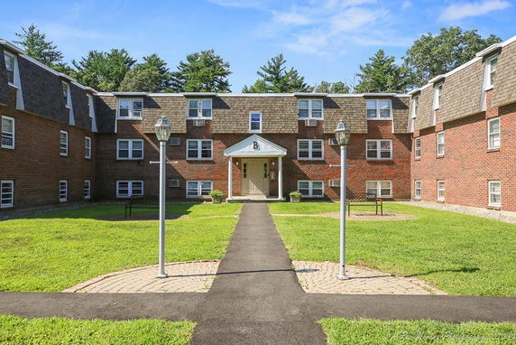 Front view of a three-story apartment complex with brick facade and pitched roof.