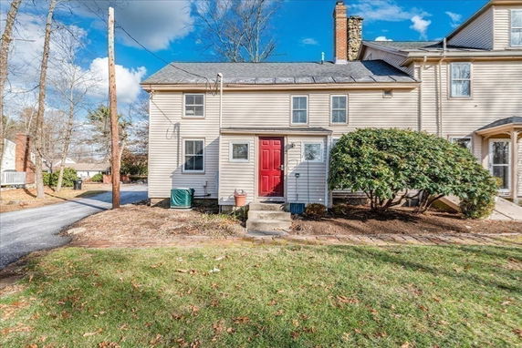 Front view of a two-story house with a red door and adjacent greenery.