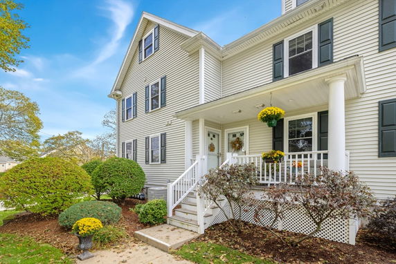 Front view of a two-story house with a porch and hanging plants.