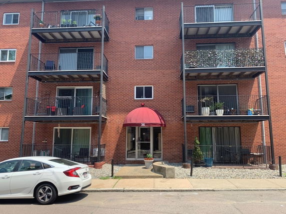 Front view of a multi-story brick apartment building with balconies and a red awning over the entrance.