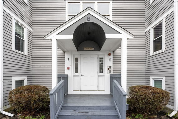 Entrance view of a gray apartment building with a covered porch and double doors.