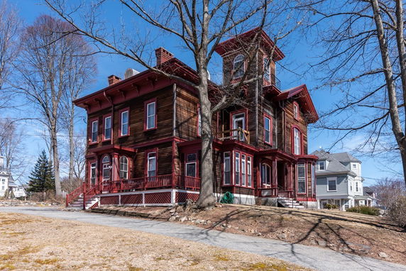 Front view of a two-story wooden house with red trim and multiple windows.